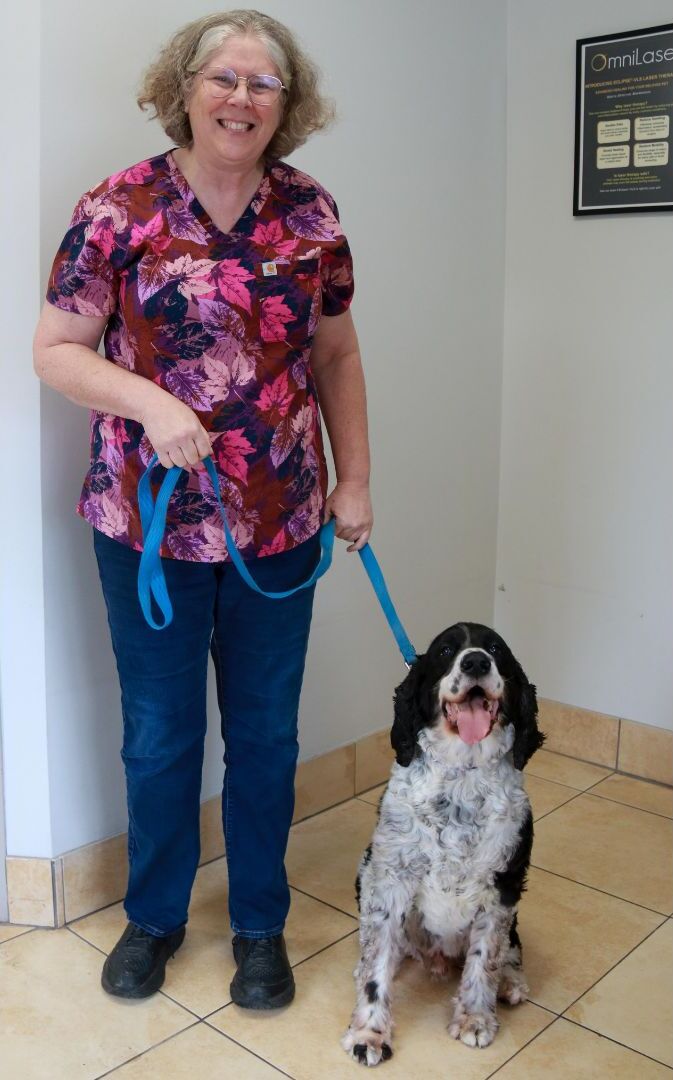 A person in scrubs smiles while holding the leash of a black and white dog. A person in scrubs smiles while holding the leash of a black and white dog.